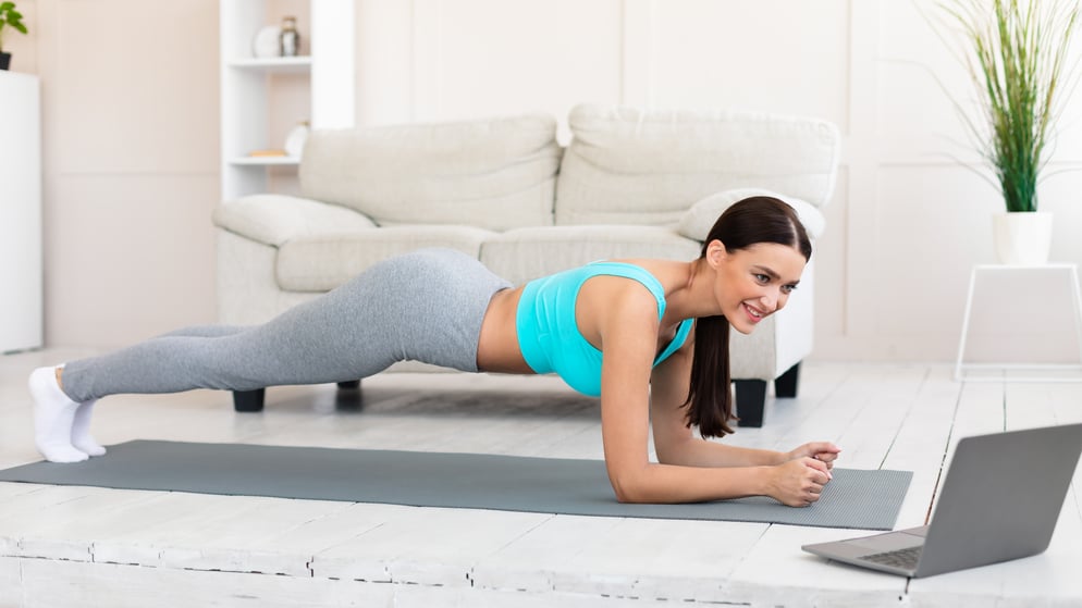 young-woman-at-laptop-exercising-doing-plank-durin-QKAWFD8